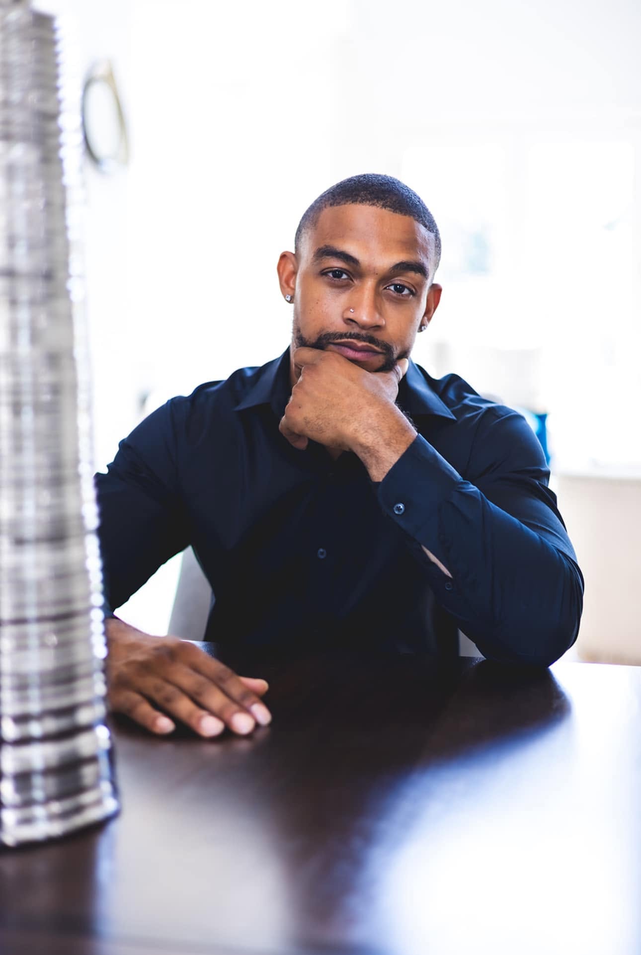 Man in a navy shirt, chin on hand, in soft window light