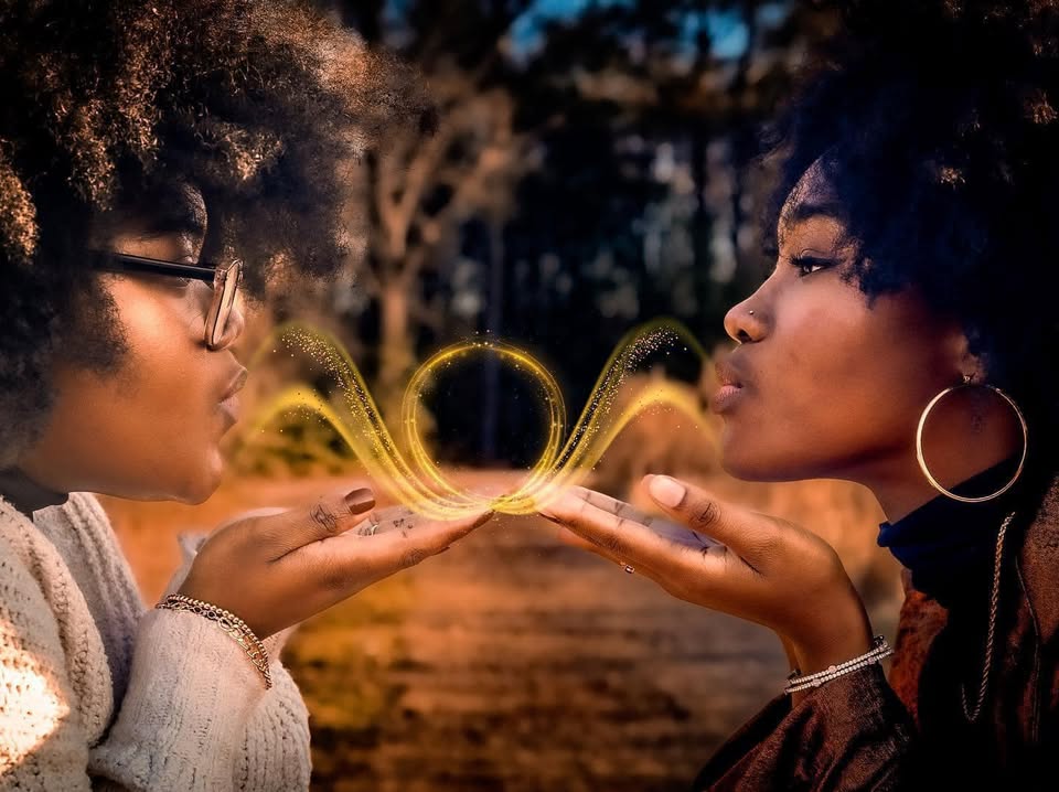 Two women blowing a golden infinity of light between their hands