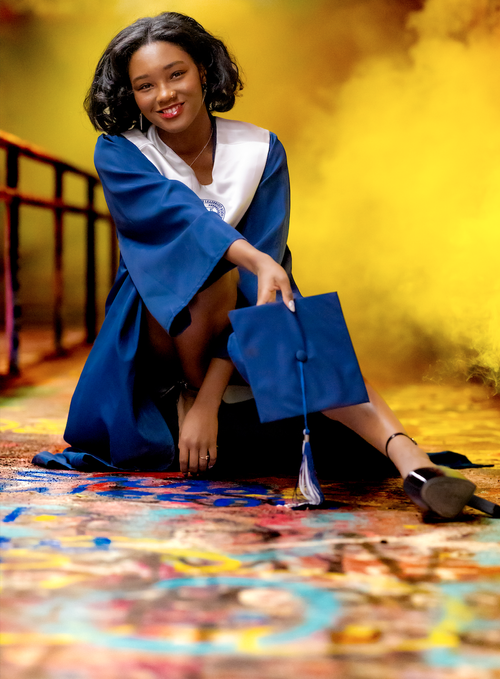 Smiling graduate in navy seated on a painted bridge in golden smoke