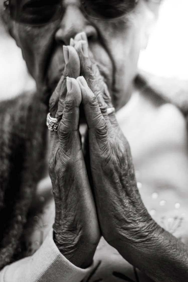 Elder's weathered hands pressed together in prayer, black and white