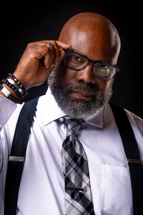 Man in glasses and suspenders adjusting his frames on black