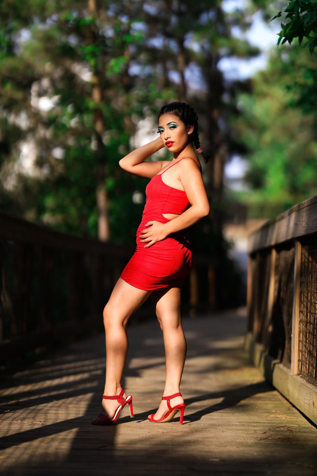 Woman in a red dress and heels posing on a forest boardwalk