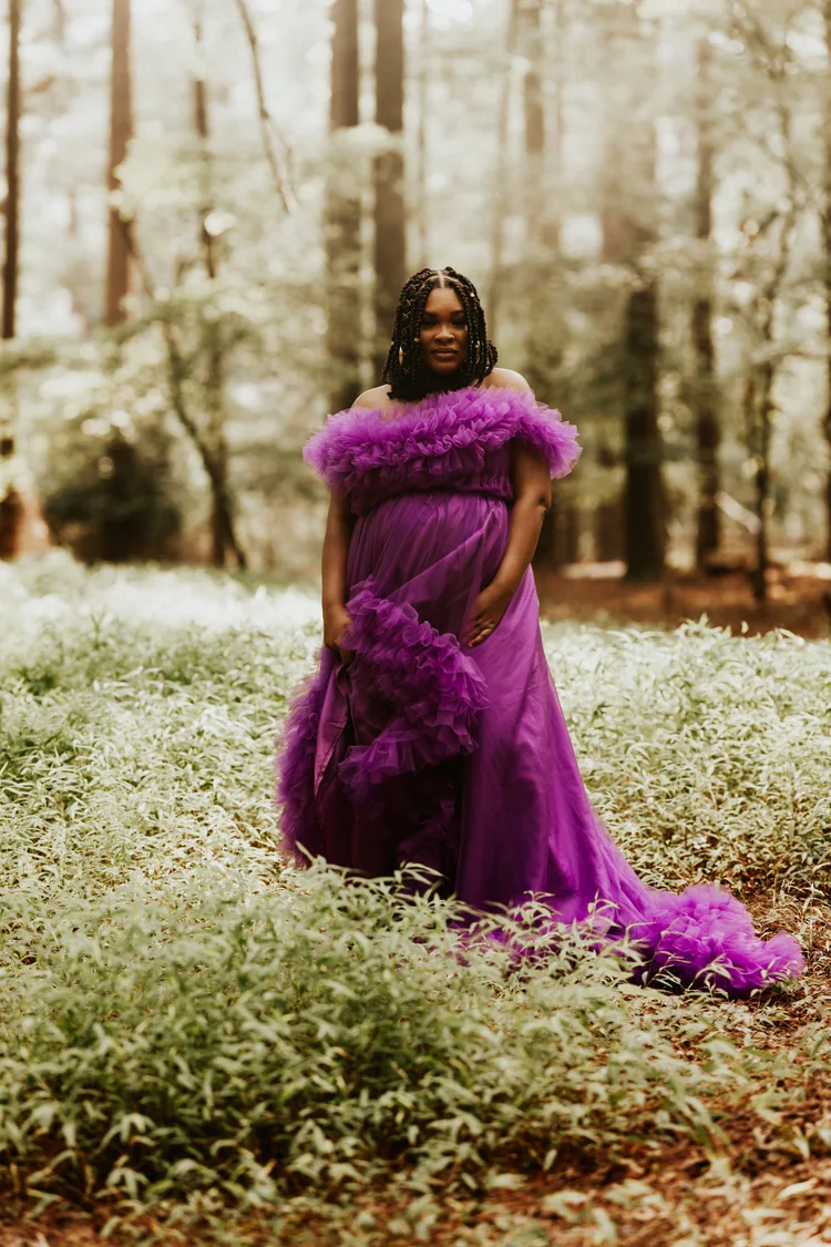 Mother-to-be in a ruffled purple gown standing in a forest