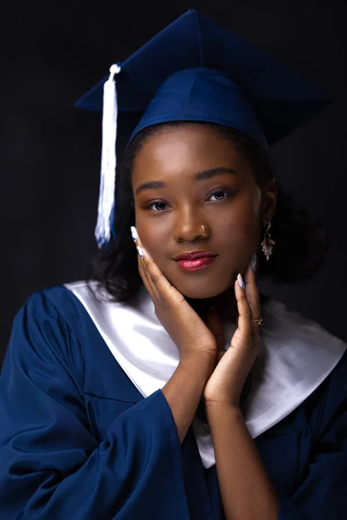 Graduate in a navy cap and gown framing her face with her hands