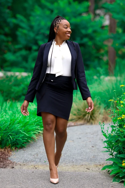 Woman in a navy skirt suit walking a garden path, glancing aside