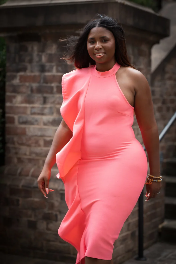 Woman in a coral ruffle dress striding past brick