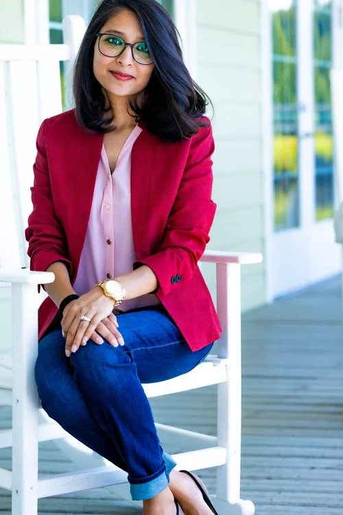 Woman in a red blazer and glasses on a white porch chair