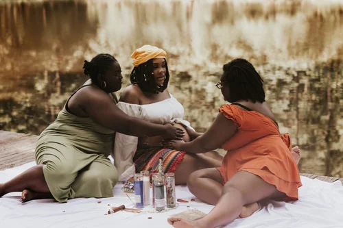 Friends laying hands on a mother-to-be at a lakeside blessing