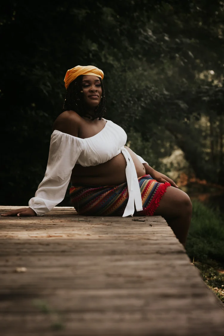Woman in a marigold headwrap seated on a wooden boardwalk