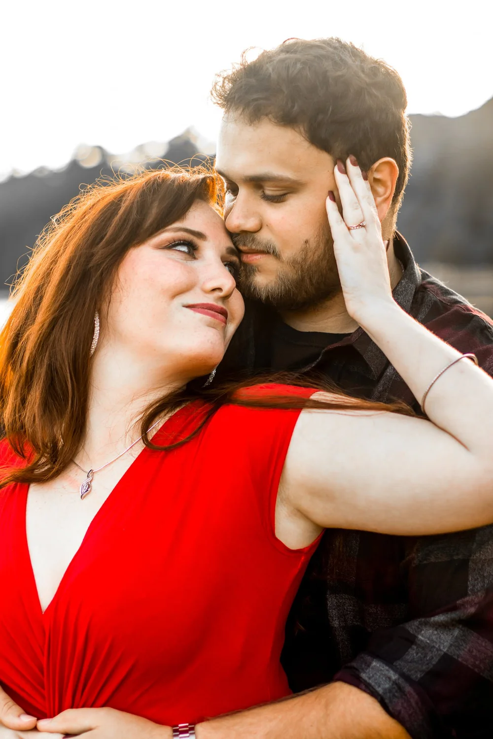 Woman in a red dress leaning back into her partner's embrace at golden hour