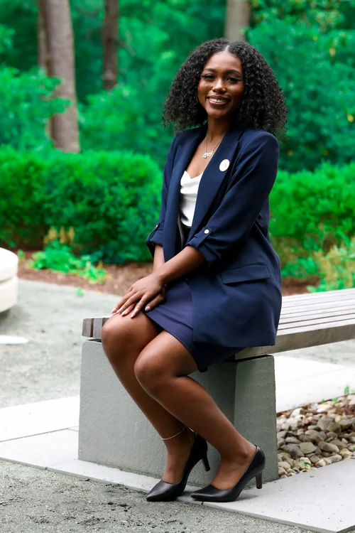 Woman in a navy suit seated on a stone bench among greenery