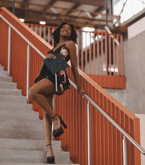 Graduate in a floral romper and platform heels posing on an orange stairway