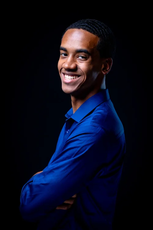 Young man in a cobalt shirt smiling over his shoulder on black