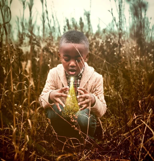 Young boy cupping a glowing golden cone in tall grass