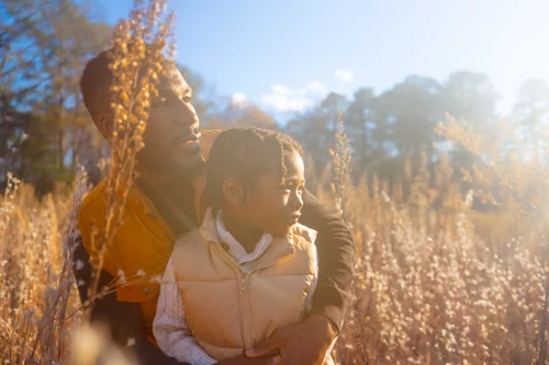 Father holding his daughter in a sunlit golden field