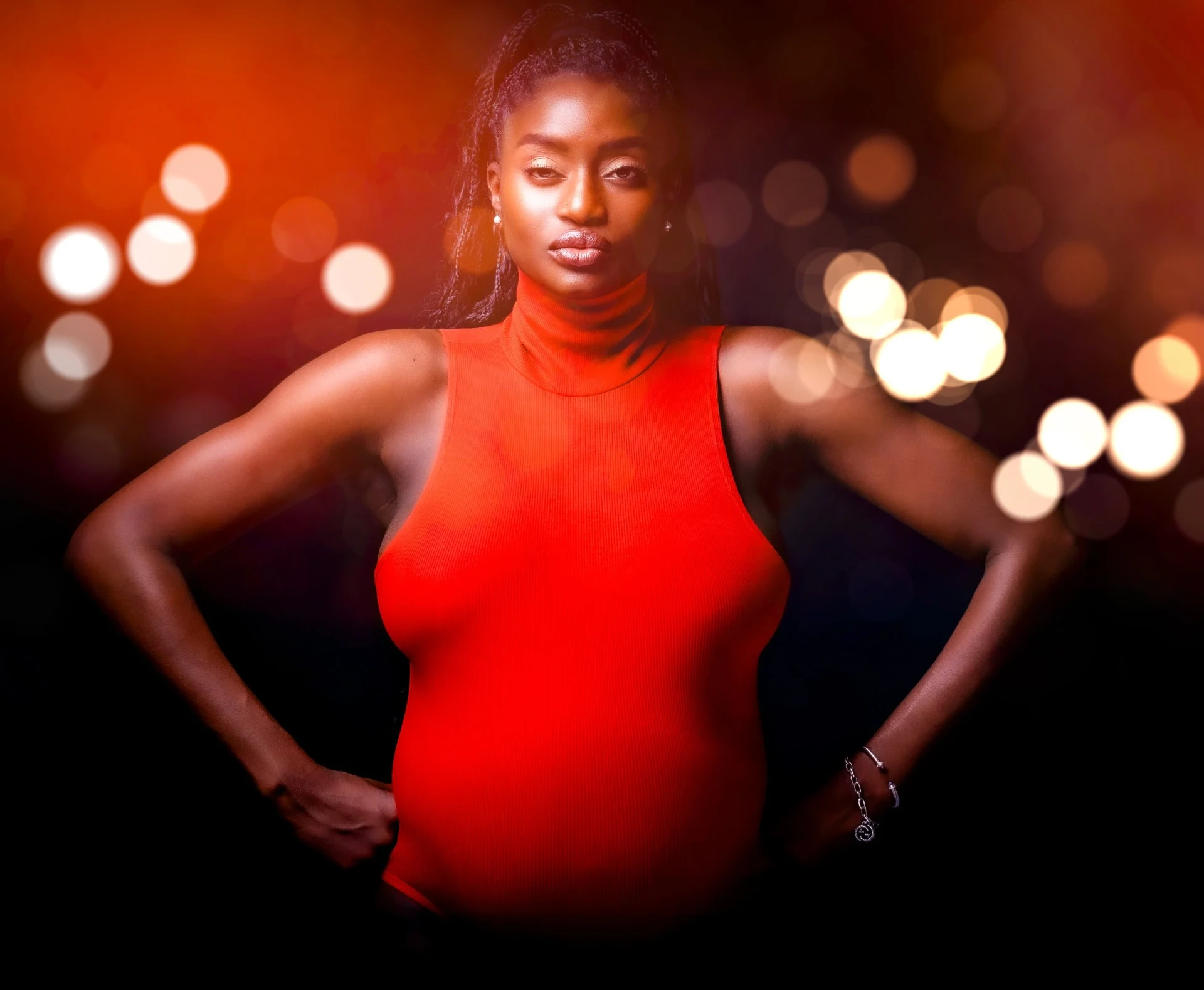 Woman in an orange top, hands on hips, against warm bokeh