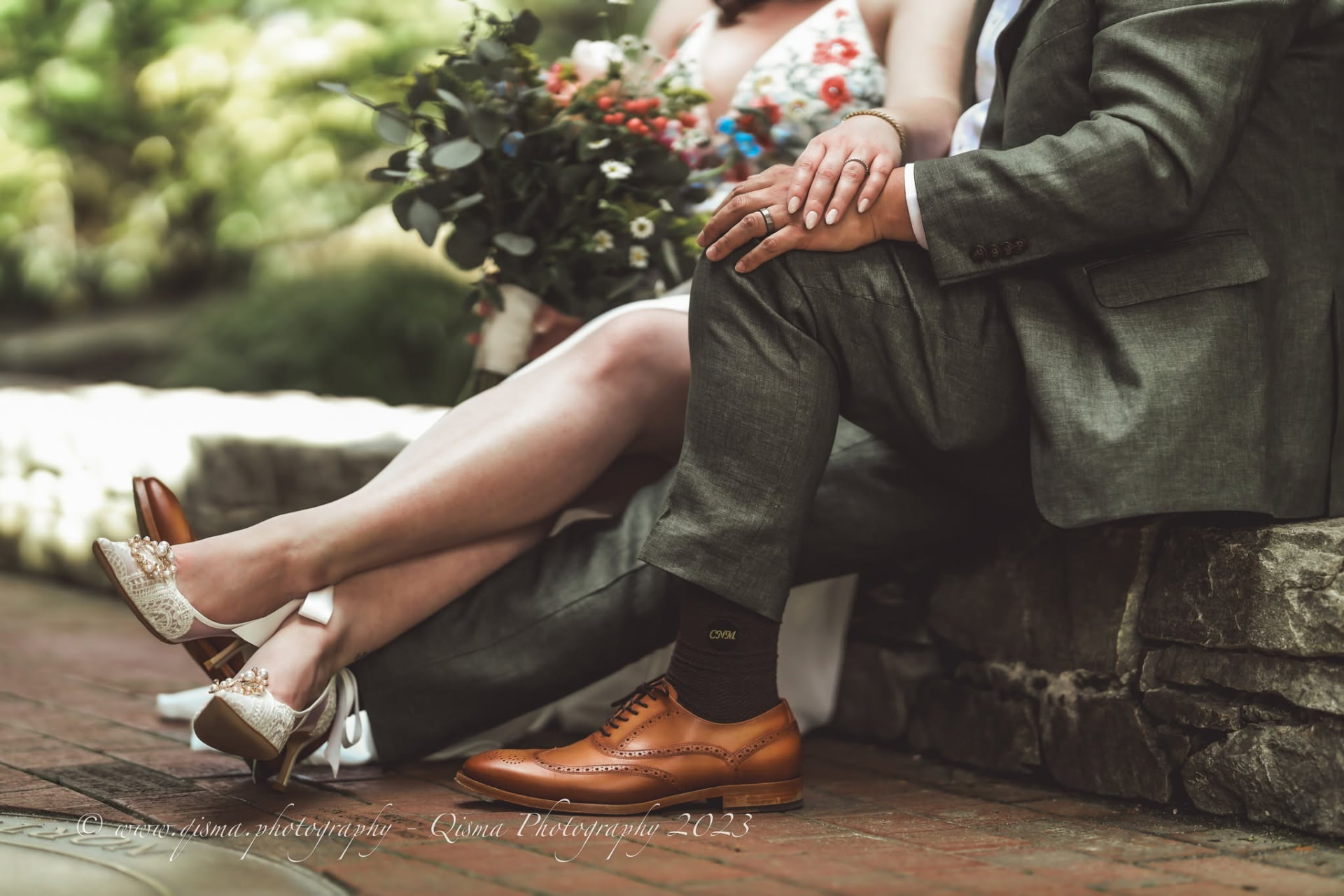 Newlyweds seated on a stone wall, bouquet and brogues in frame
