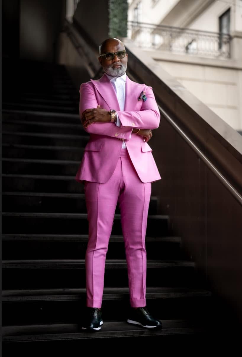Man in a pink suit, arms crossed, at the foot of a dark stairway