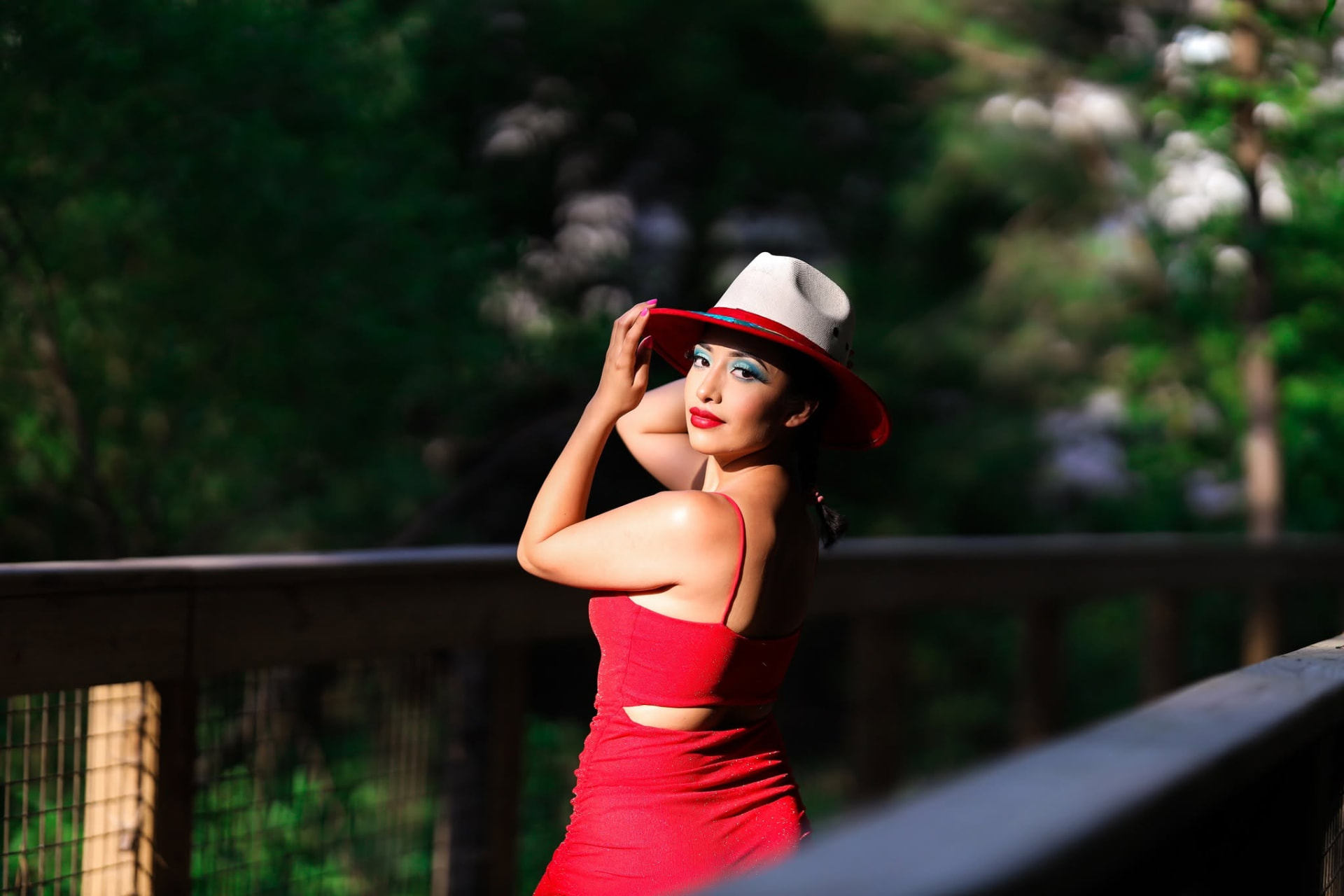 Woman in a red dress and red-brimmed hat by a wooden railing