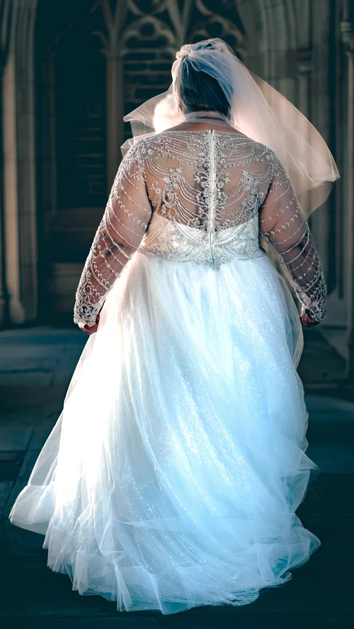 Bride from behind in a lace gown and veil, walking into the light