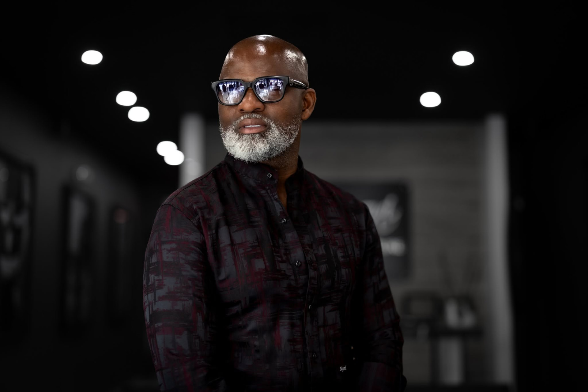 Designer in tinted glasses and a patterned shirt in low light — Editorial portrait by Claudia Quiana