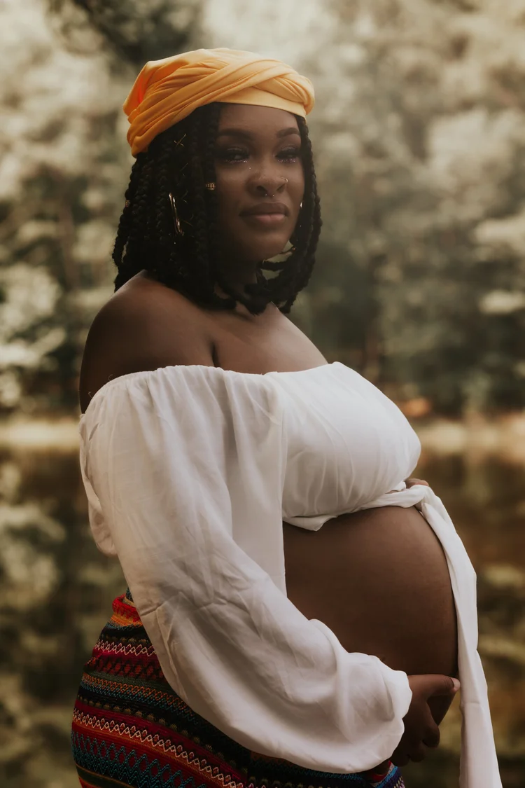 Mother-to-be in a golden headwrap and white blouse by the water