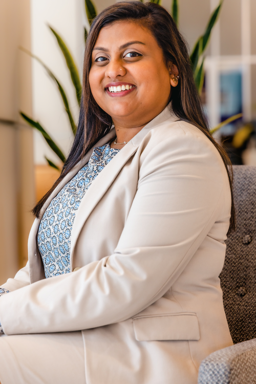 Smiling woman in a cream blazer seated by a window