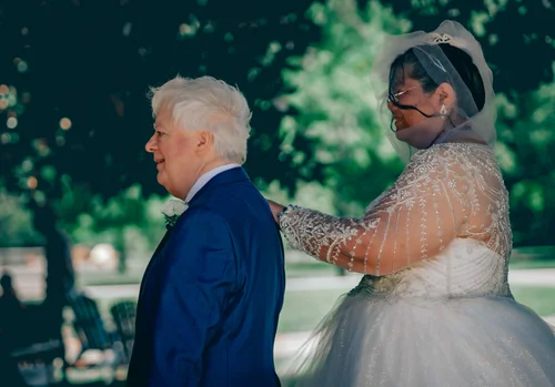 Bride touching her partner's shoulder for the first look under the trees