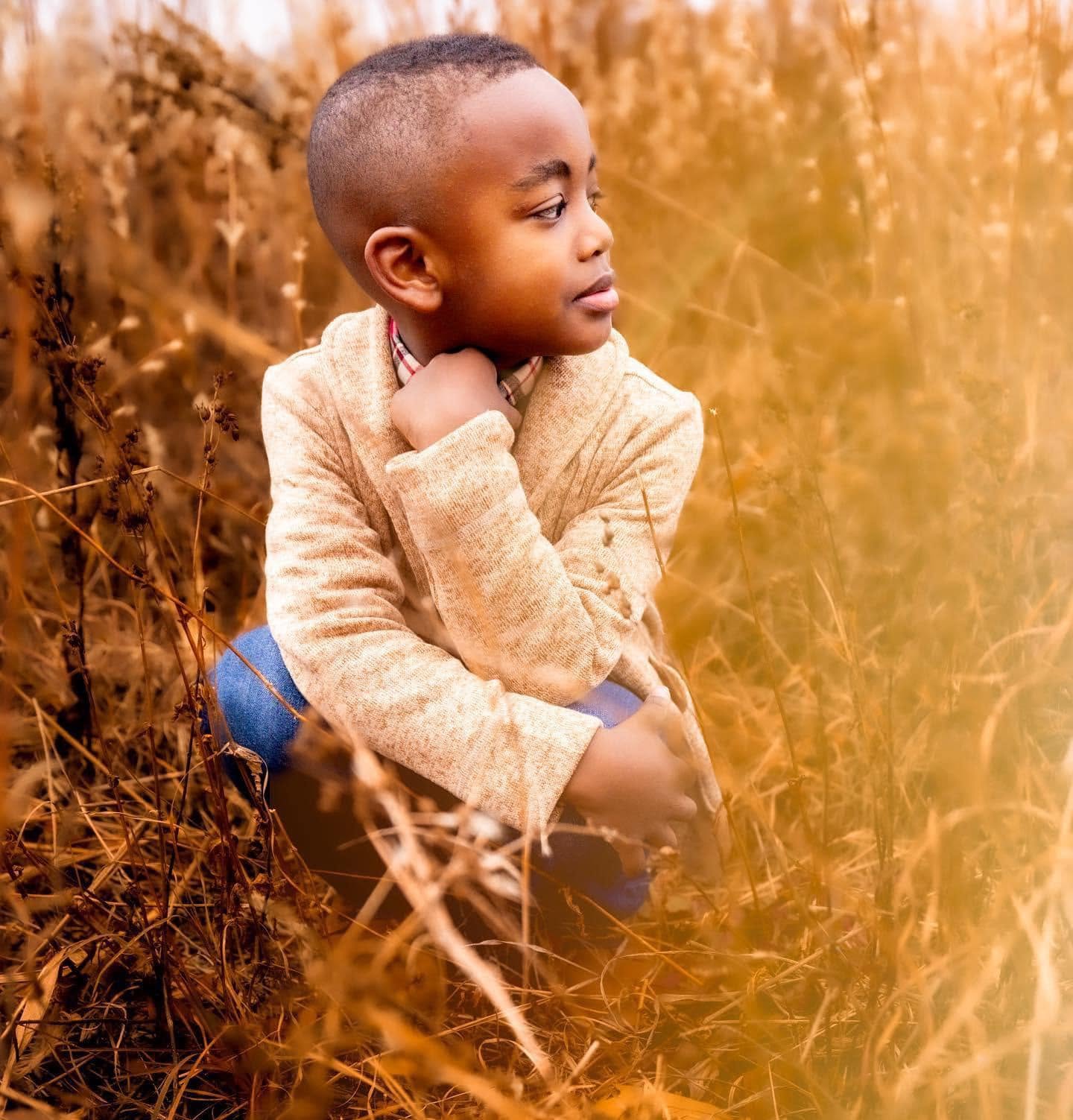 Young boy crouched in tall golden grass, looking away