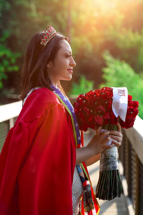 Graduate in a red gown and tiara in profile with red roses