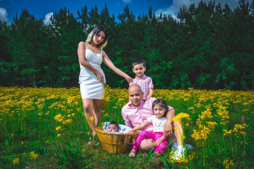 Family with a newborn in a basket among yellow wildflowers