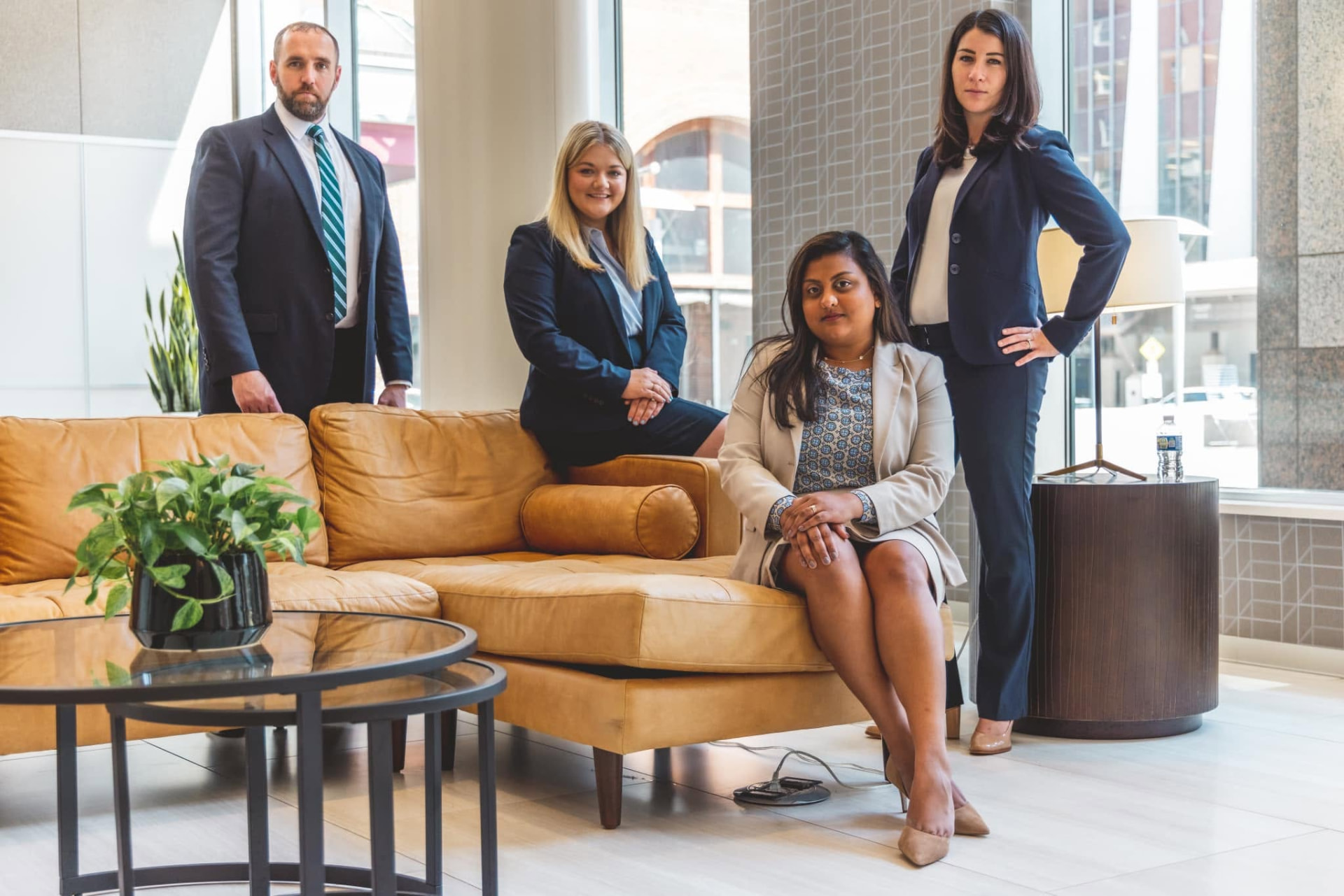 Four colleagues posed around a tan leather sofa in a bright lounge