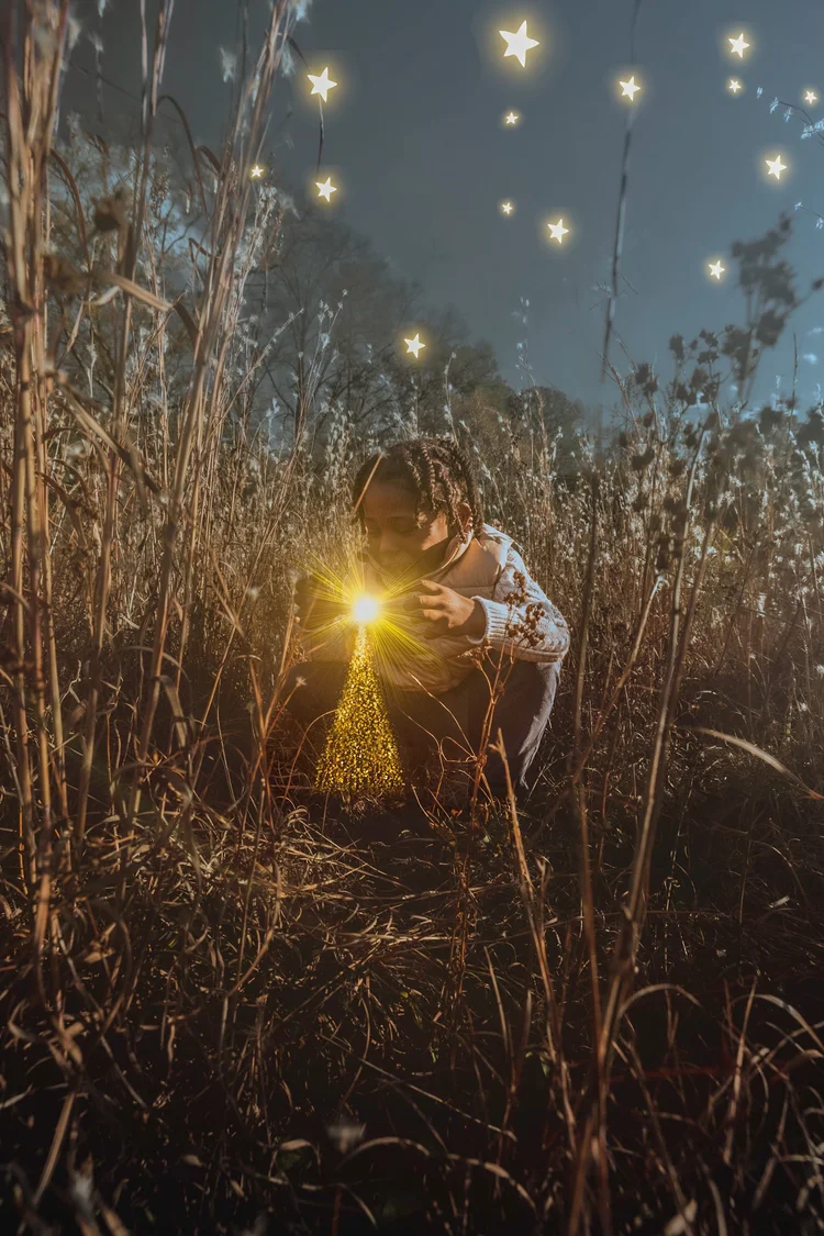 Boy crouched in tall grass under a starry dusk, cradling a glowing light