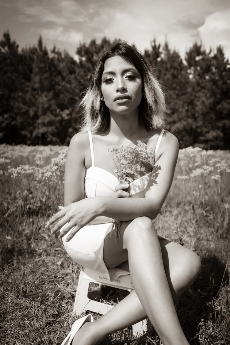 Black and white portrait of a woman in white holding wildflowers in a meadow — Editorial lifestyle portrait by Claudia Quiana