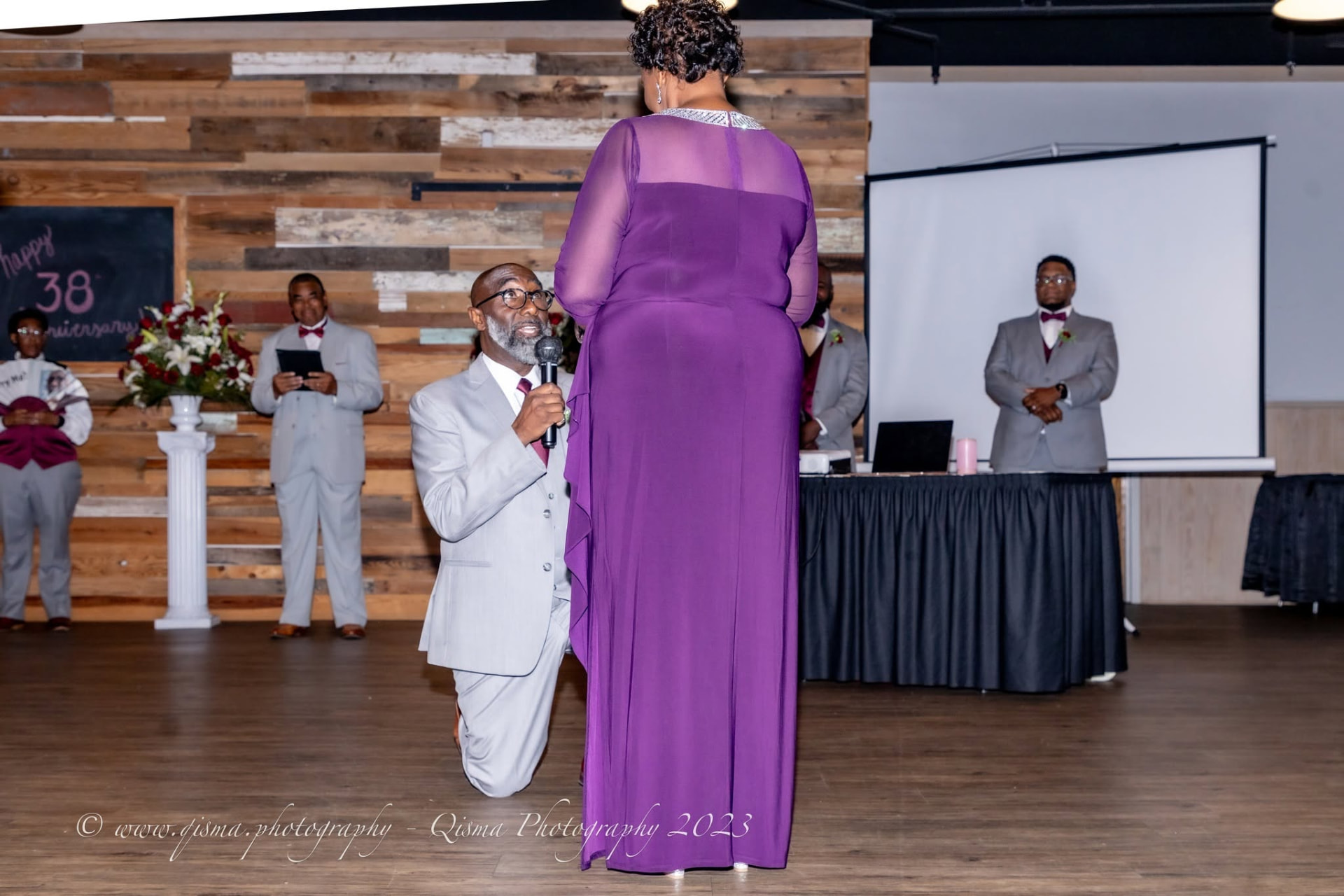 Groom kneeling to his bride in purple during a vow renewal