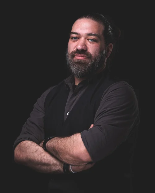 Bearded man with arms crossed in low light