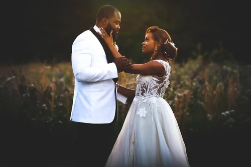 Groom in a white tux cradling his bride's face at dusk