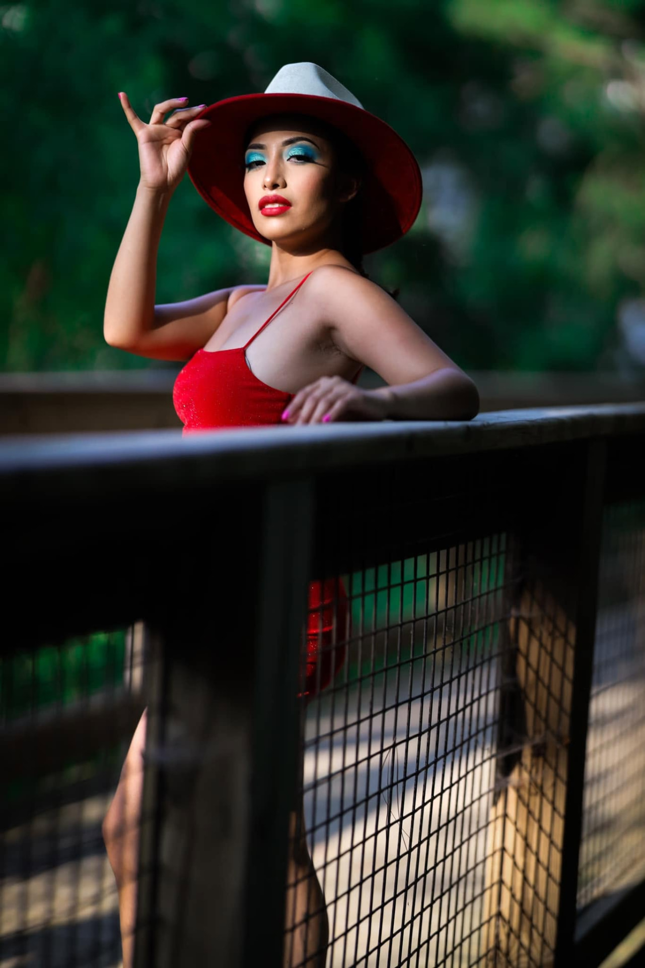 Woman in red and a red-brimmed hat leaning on a balcony rail