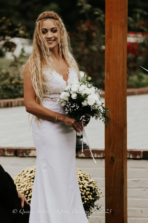 Smiling bride with her bouquet beside a wooden post