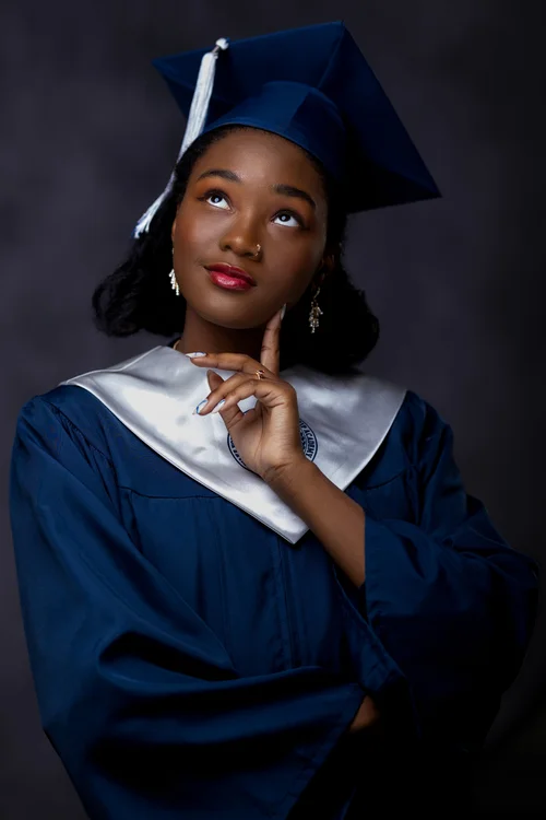 Graduate in a navy cap and gown gazing upward in the studio