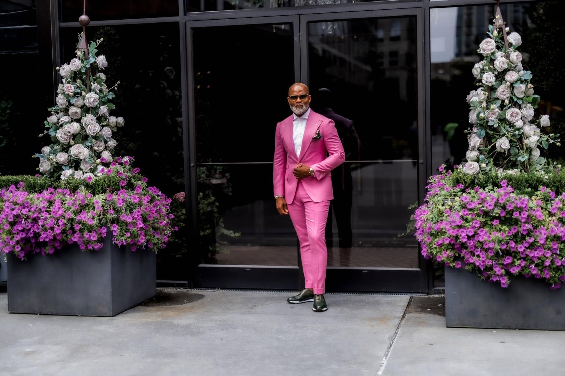 Man in a pink suit framed by rose and petunia planters at his storefront