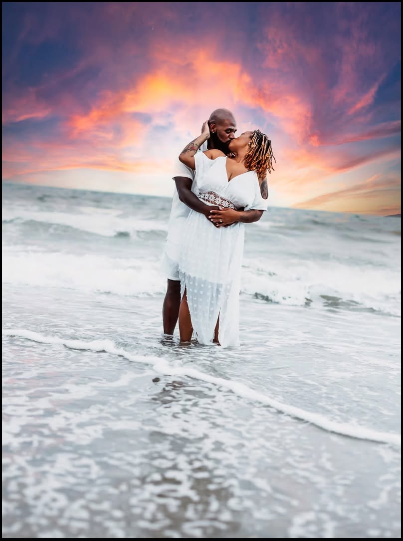 Couple in white kissing in the surf under a blazing sunset sky