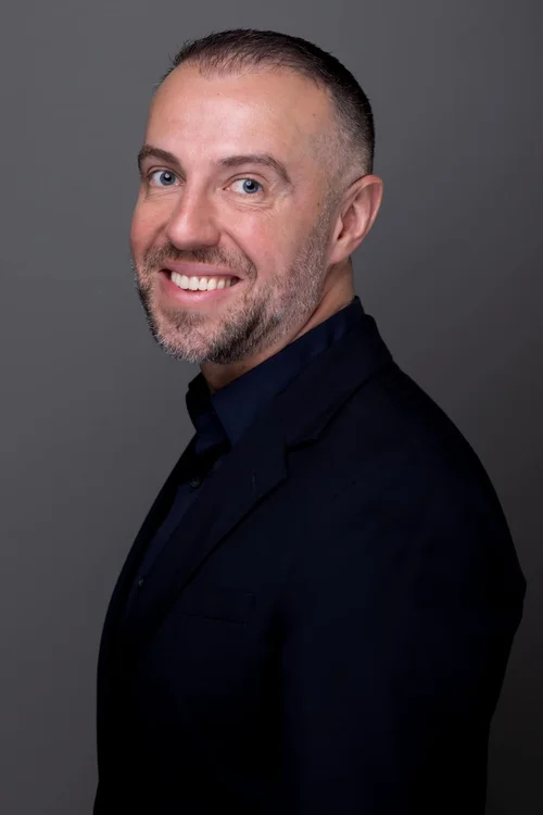 Smiling man in a dark shirt on a grey studio backdrop
